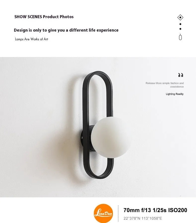 Modern minimalist wall lamp with black iron arm and clear glass shade, mounted on a plain wall.