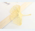 Detailed brass bookmark with hollow maple leaf pendant and rose gold tassel on a book page.