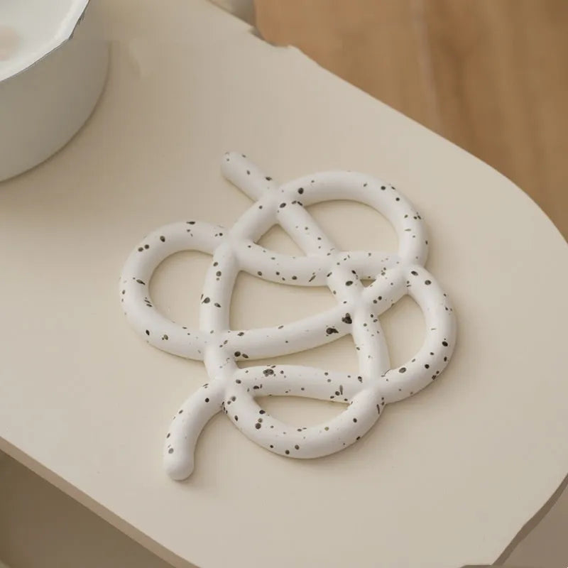 Irregular-shaped ceramic heat proof mat in grey with a curved hook for hanging, sitting on a wooden table.