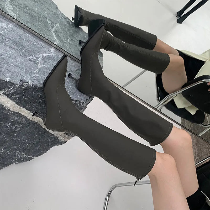 Women's black pointed toe below-the-knee boots with a stiletto heel and back zip on a neutral background.