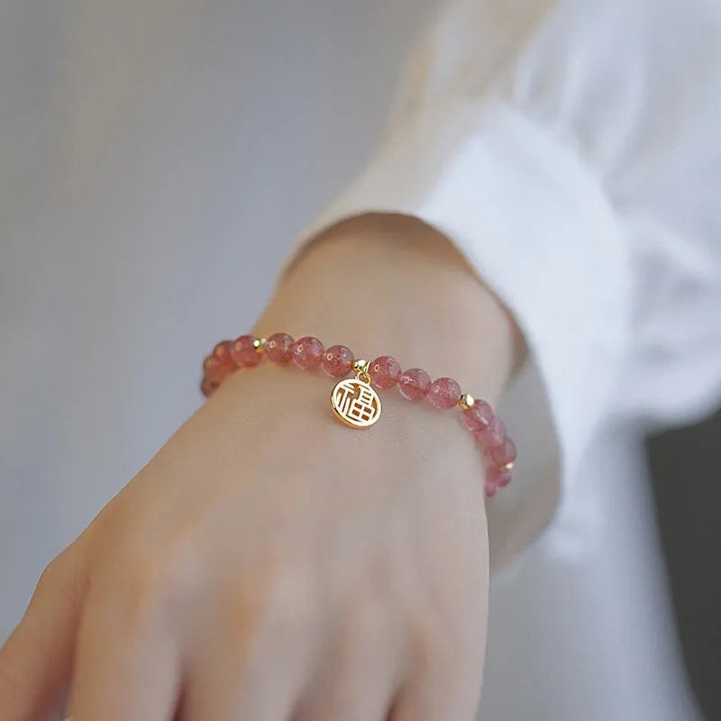 Glass strawberry quartz bead bracelet with a blessing card charm on a wrist.