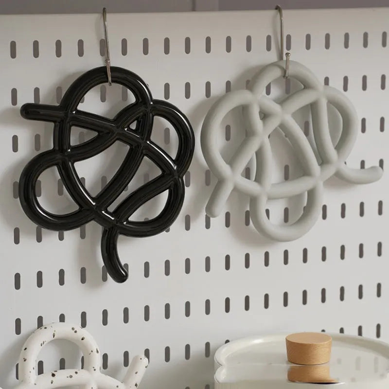 Irregular-shaped ceramic heat proof mat in grey with a curved hook for hanging, sitting on a wooden table.