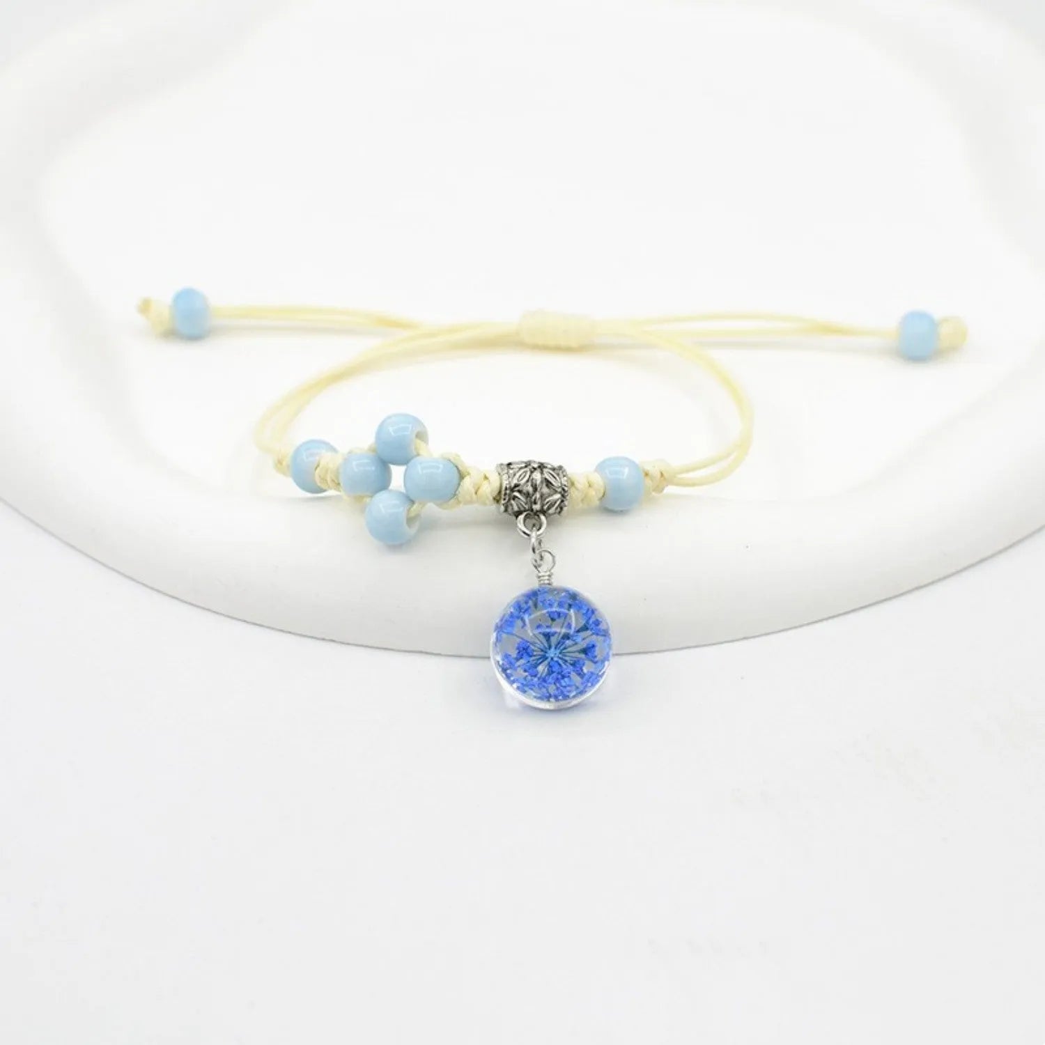 Close-up of a hand-woven glass bracelet with large 1.4cm beads containing real dried flowers and lace floral detailing.