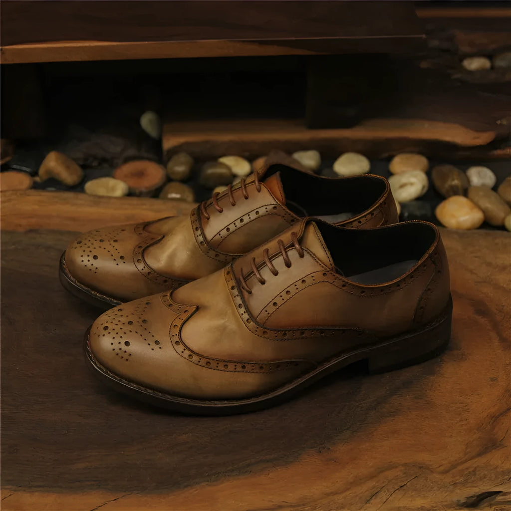 Light brown men's distressed leather lace-up shoes on a wooden surface, showing hand-carved details and round toe design.