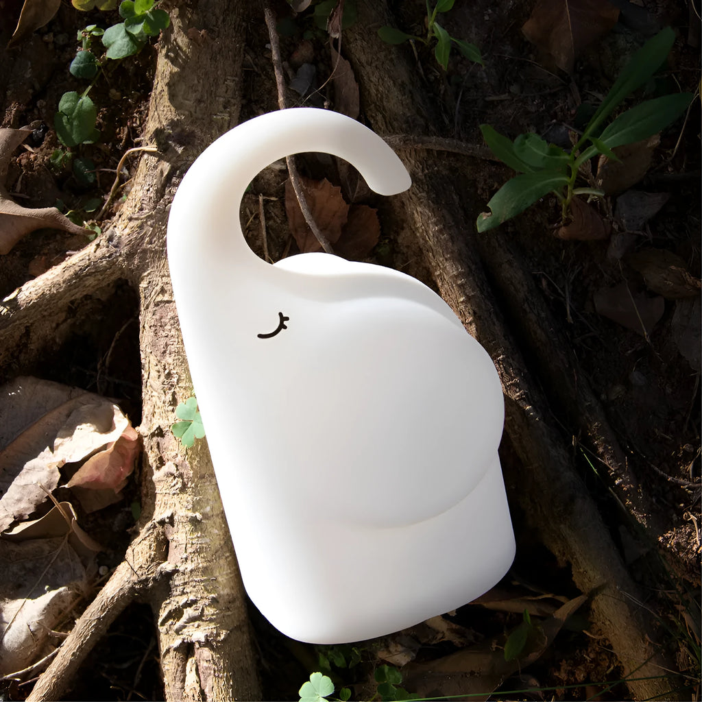 DOMI Elephant shaped silicone night light with warm white glow on a bedside table.