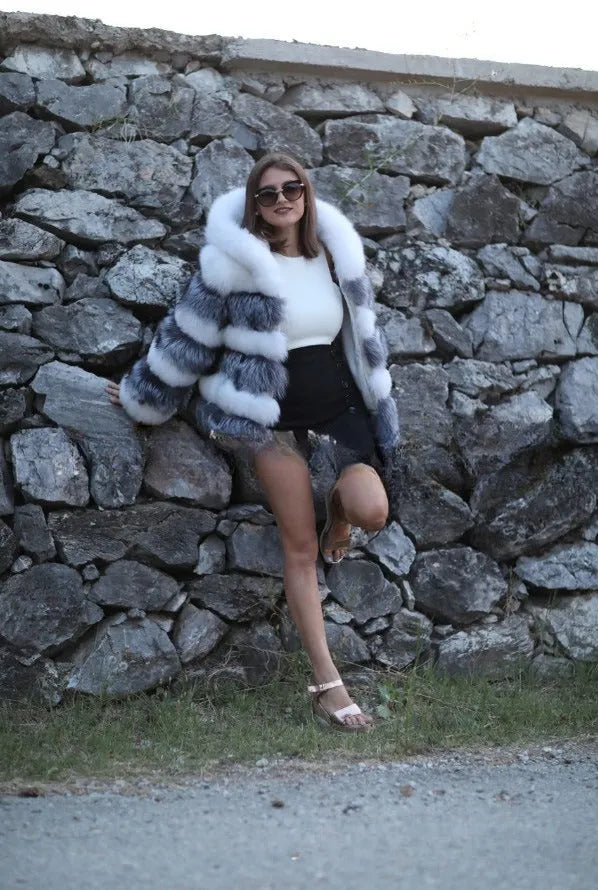 A woman modelling a loose-fitting, hooded artificial fur coat in a street fashion style.