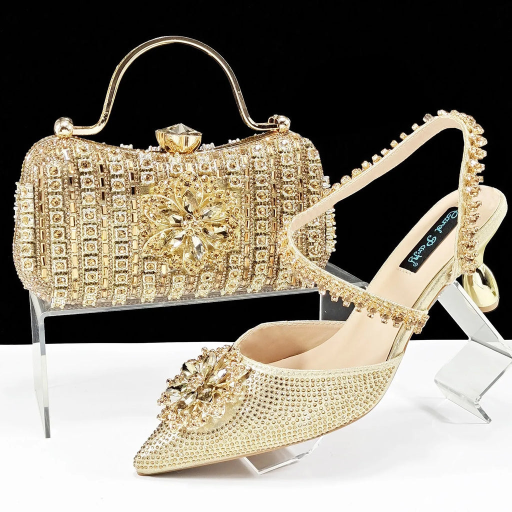 Women's black high heel shoes with rhinestone flowers and an ankle chain, next to a matching hard clutch bag.
