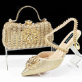 Women's black high heel shoes with rhinestone flowers and an ankle chain, next to a matching hard clutch bag.