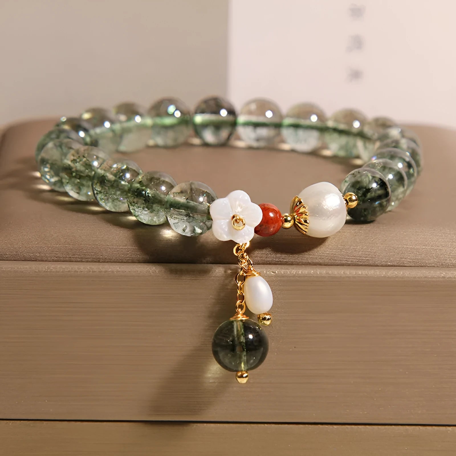 Women's green phantom quartz crystal bracelet with small shell flower accent on wrist.