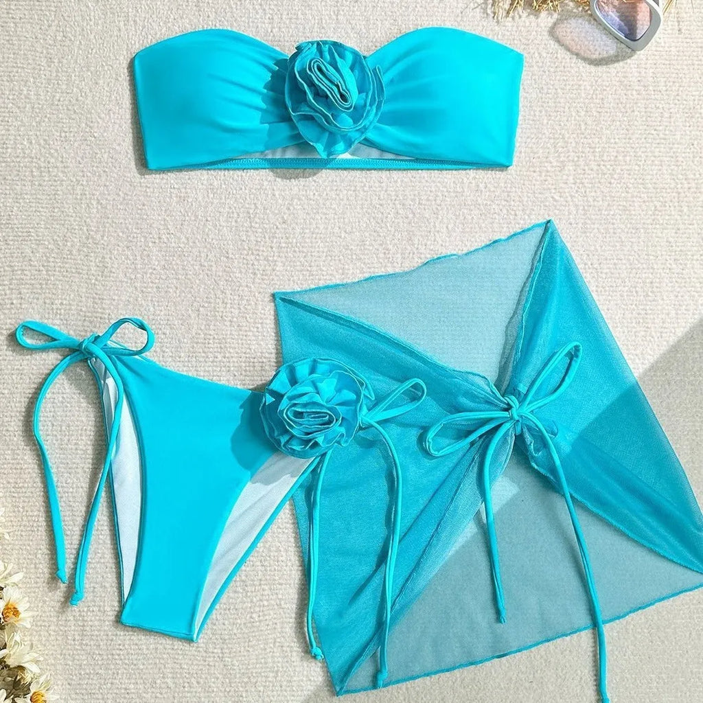 Blue women's swimsuit set with 3D flower, bikini bottoms, and a separate wrap skirt laid flat.