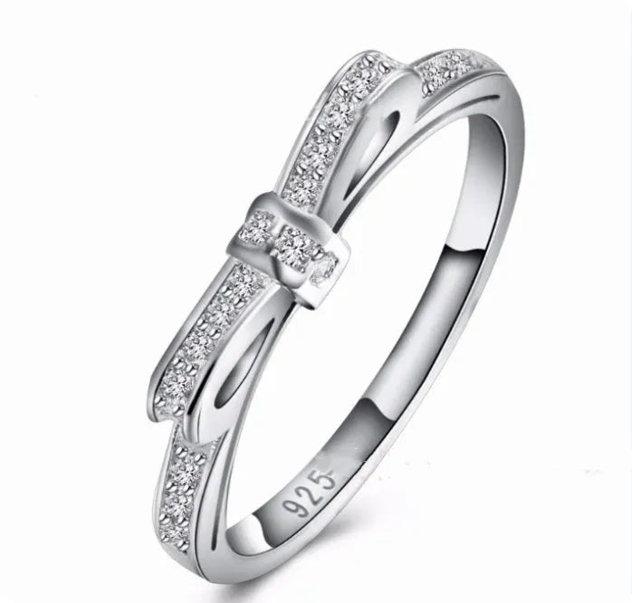 Silver coloured bow-shaped ring with sparkling rhinestone crystals on a model's hand.