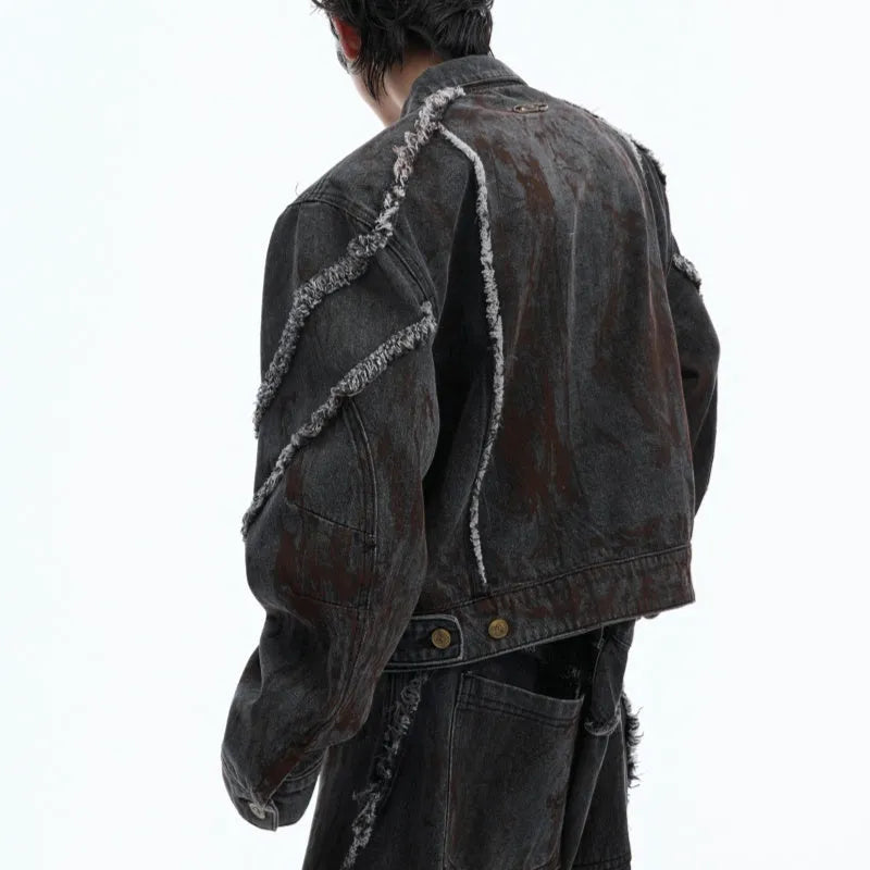 Black raw-edge splash-dye distressed denim coat with padded shoulders and matching trousers on a hanger.