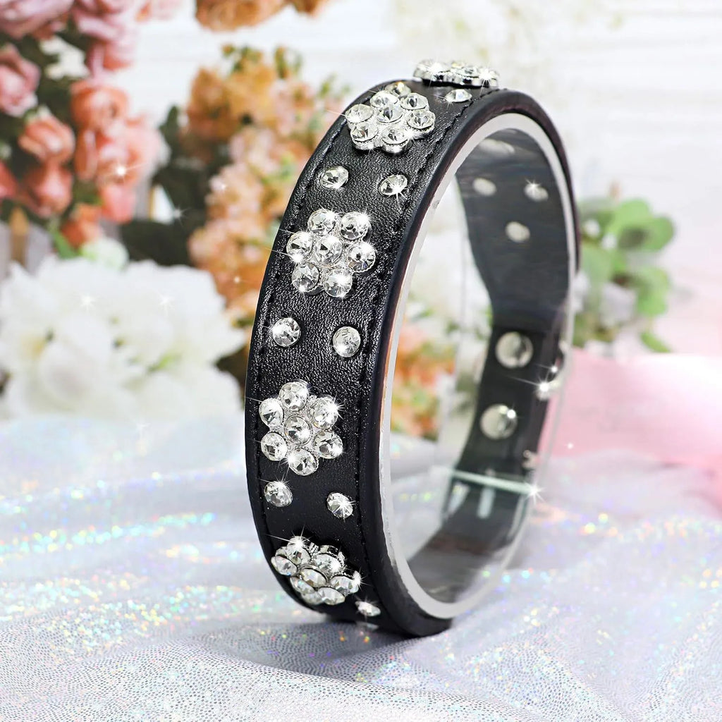 A black PU leather dog collar with glittering rhinestone flower studs and a metal D-ring.