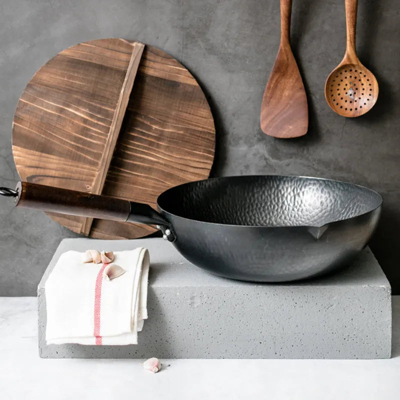 Handmade black iron wok pan with a long wooden handle on a kitchen counter.