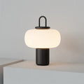 Minimalist Japanese designer glass table lamp with warm light on a bedside table.