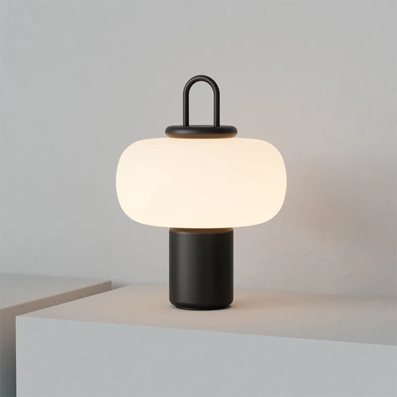 Minimalist Japanese designer glass table lamp with warm light on a bedside table.