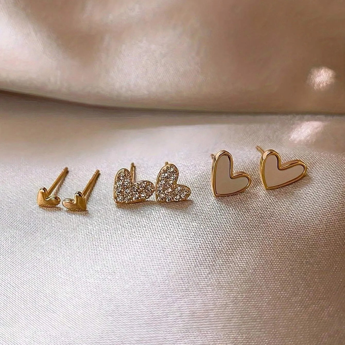 Three pairs of girly heart-shaped alloy earrings in gold, black, pink, and black and white colours.