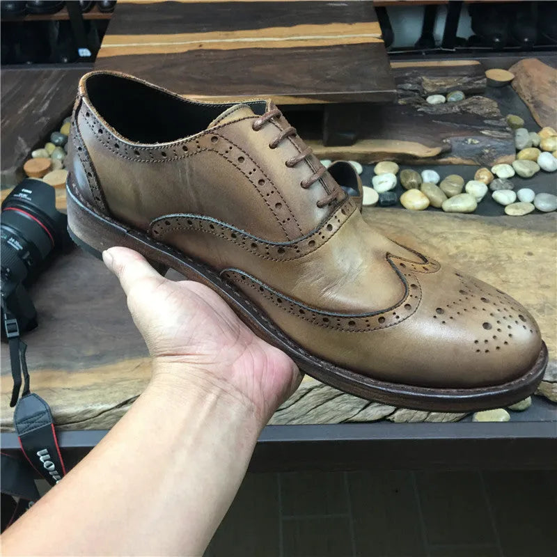 Light brown men's distressed leather lace-up shoes on a wooden surface, showing hand-carved details and round toe design.