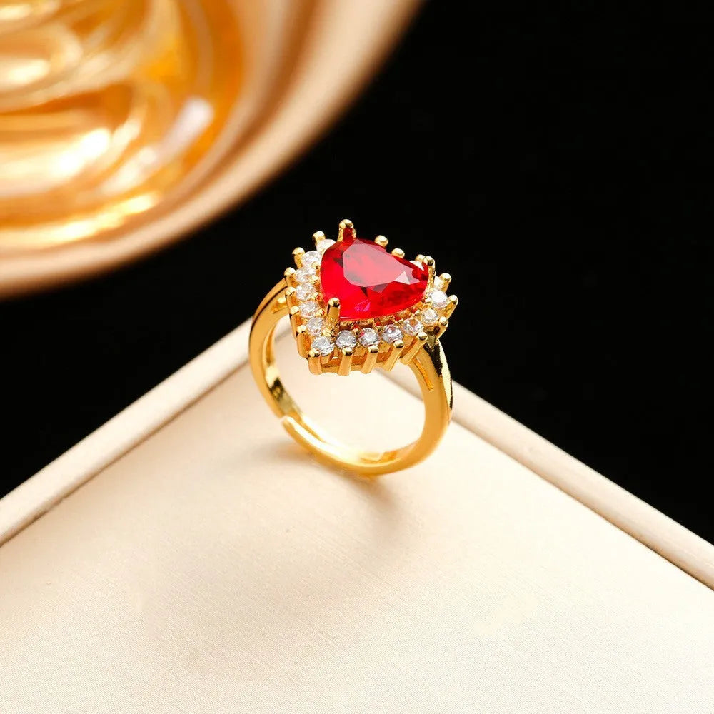 Gold red titanium steel necklace with heart and flower pendant, matching stud earrings, and ring on a grey background.