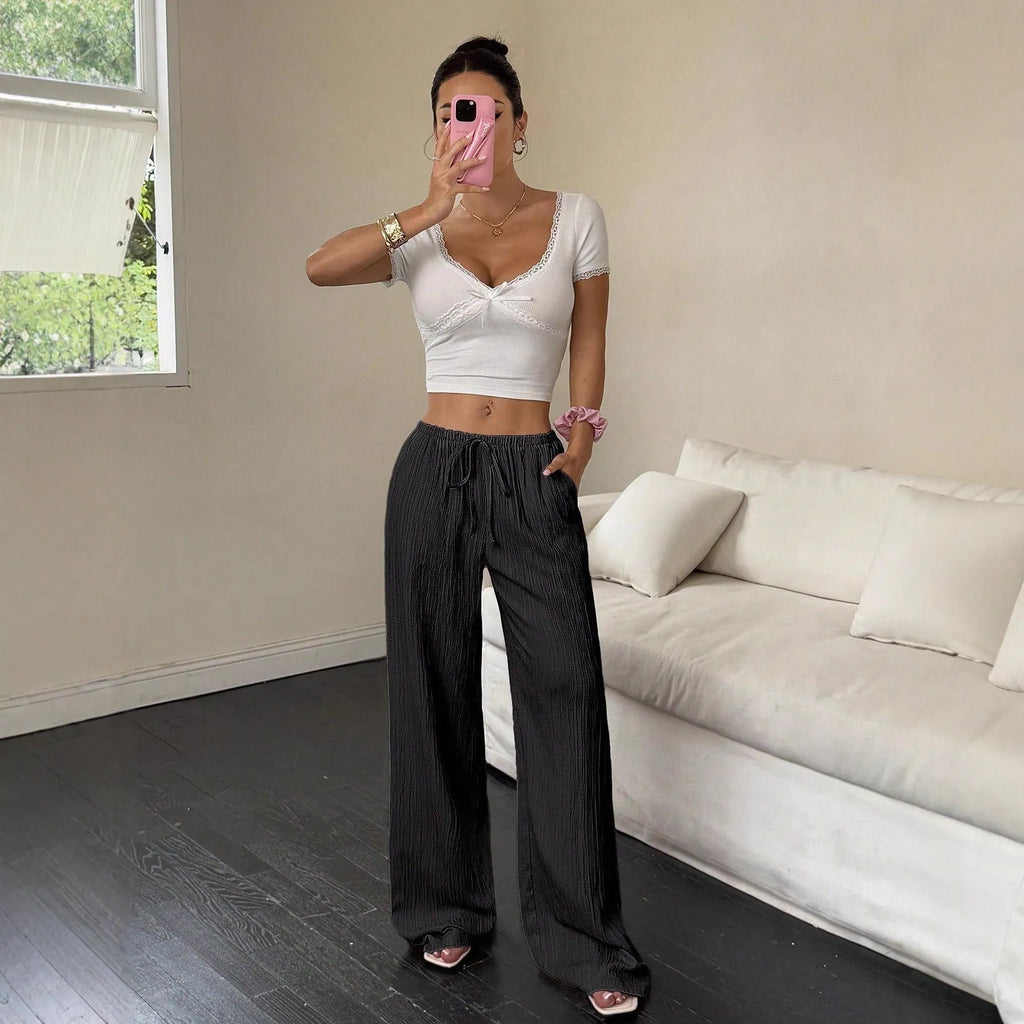 Women's black wide-leg trousers with a front lace-up waist detail on a neutral background.