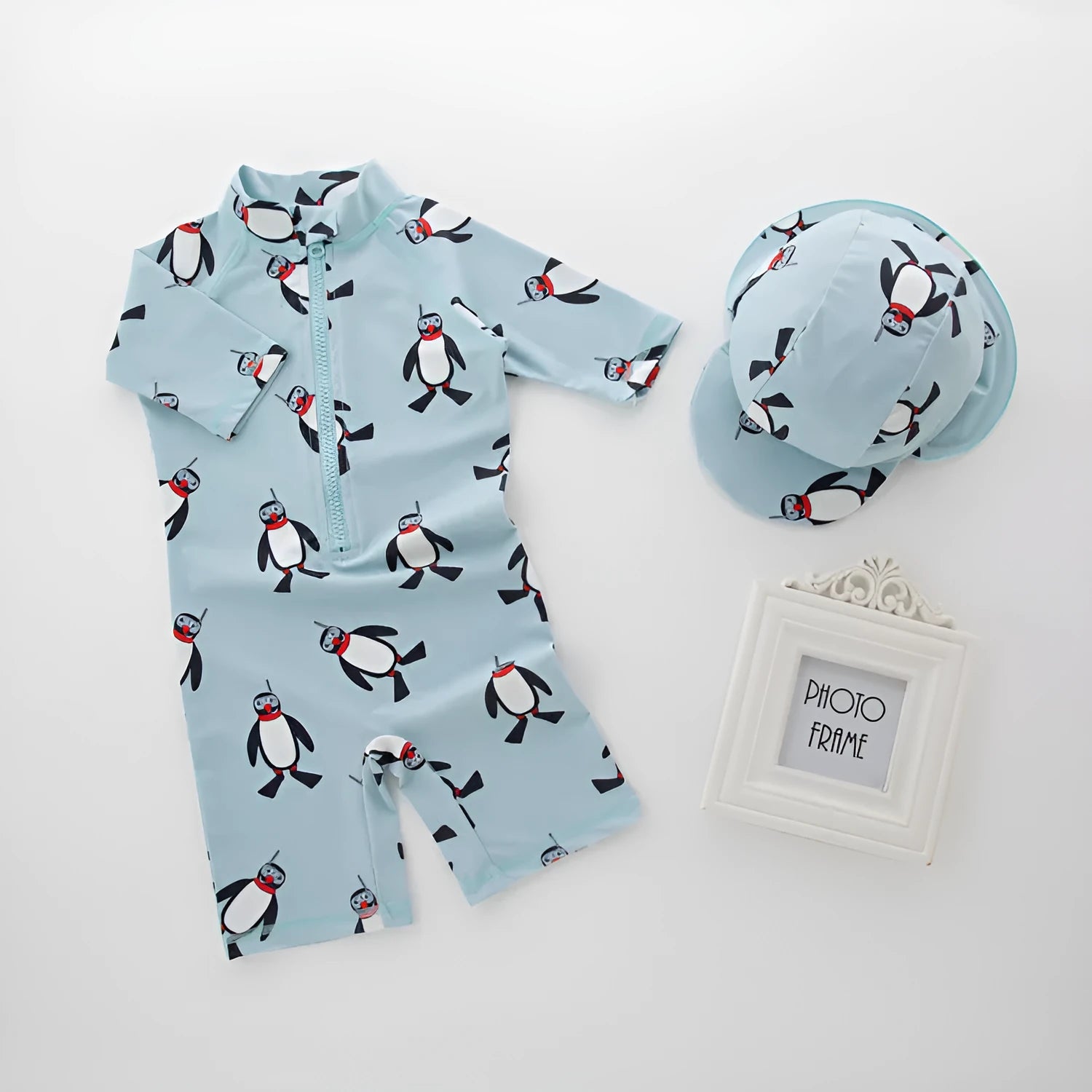 Boy's penguin print long sleeve swimsuit top and matching swim cap set on blue background