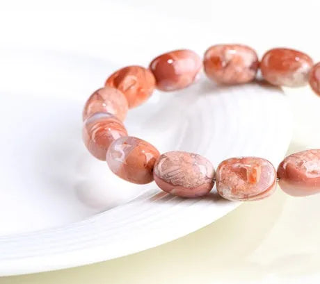 Natural cherry agate barrel bead bracelet with Ruyi charm on a wrist.
