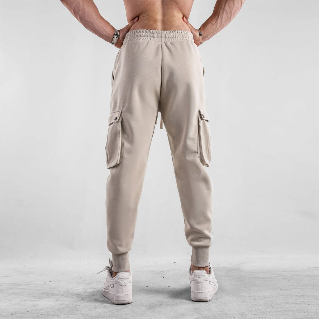 Men's loose-fit light grey cotton trousers with tapered legs and tied ankle cuffs, showing multi-pocket detail.