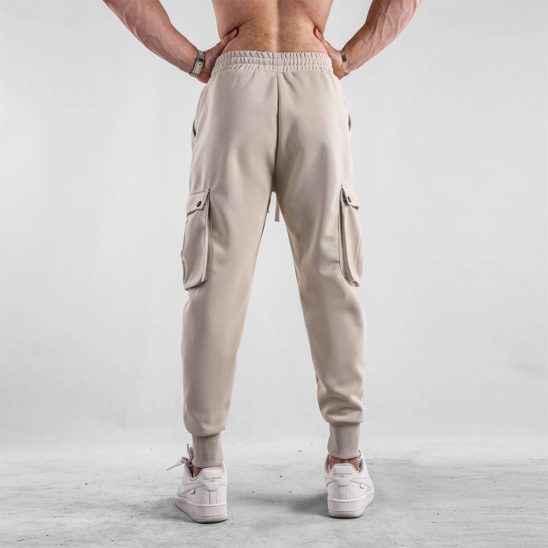 Men's loose-fit light grey cotton trousers with tapered legs and tied ankle cuffs, showing multi-pocket detail.