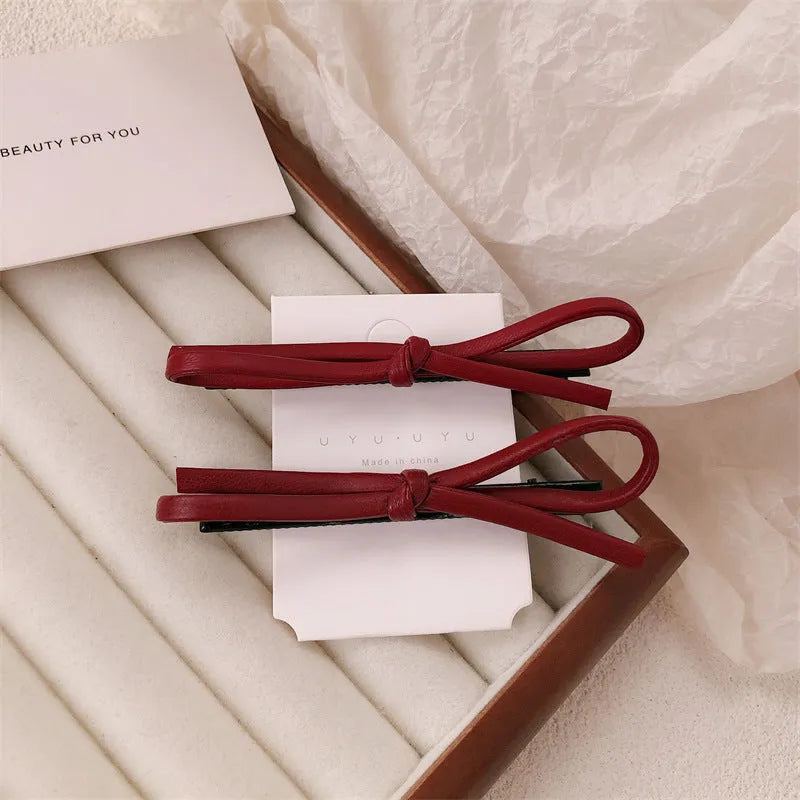 Wine red genuine leather bow hair barrette with a silver metal pinch clip on a white background.