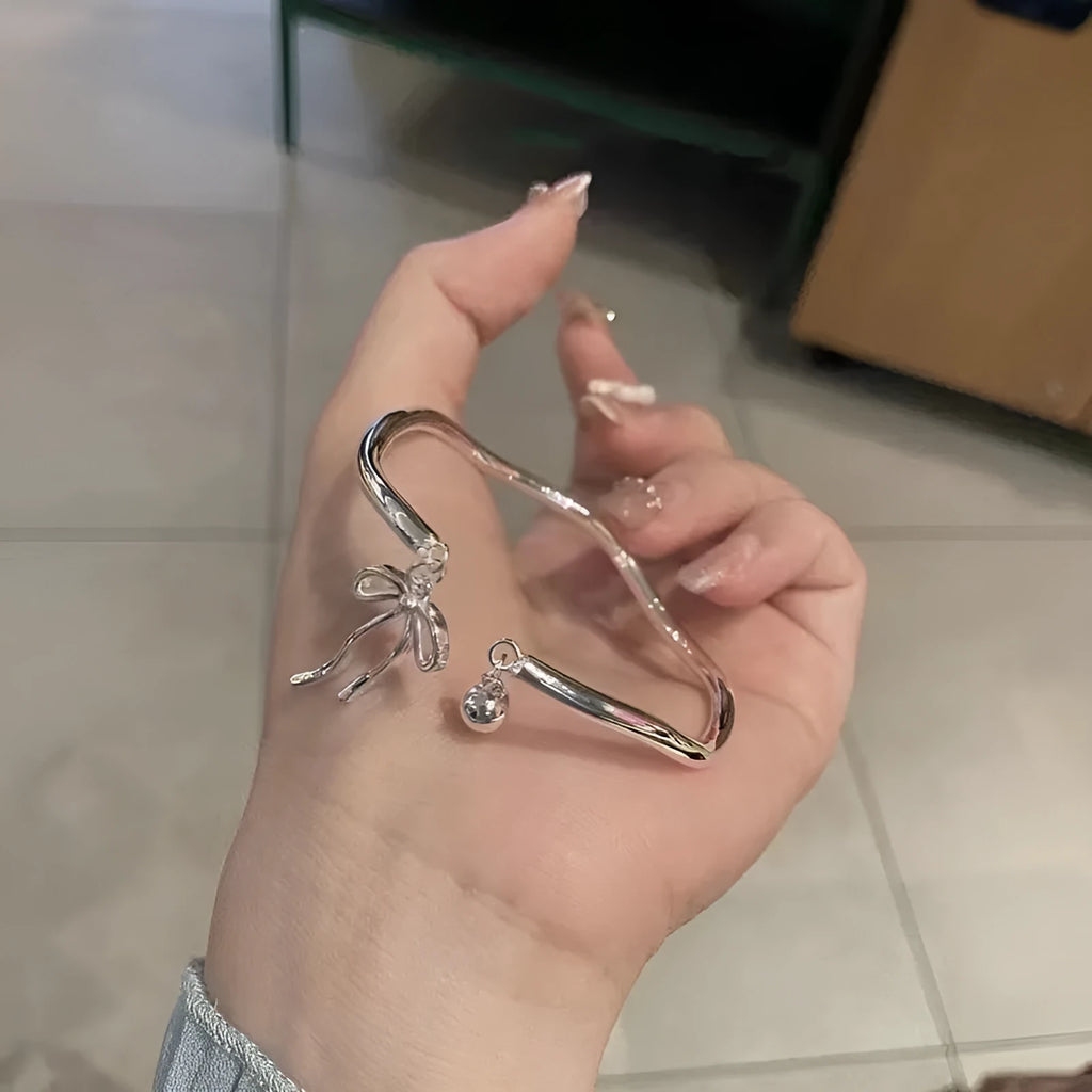 Silver adjustable bracelet with a detailed bow charm on a model's wrist, showing the adjustable clasp.