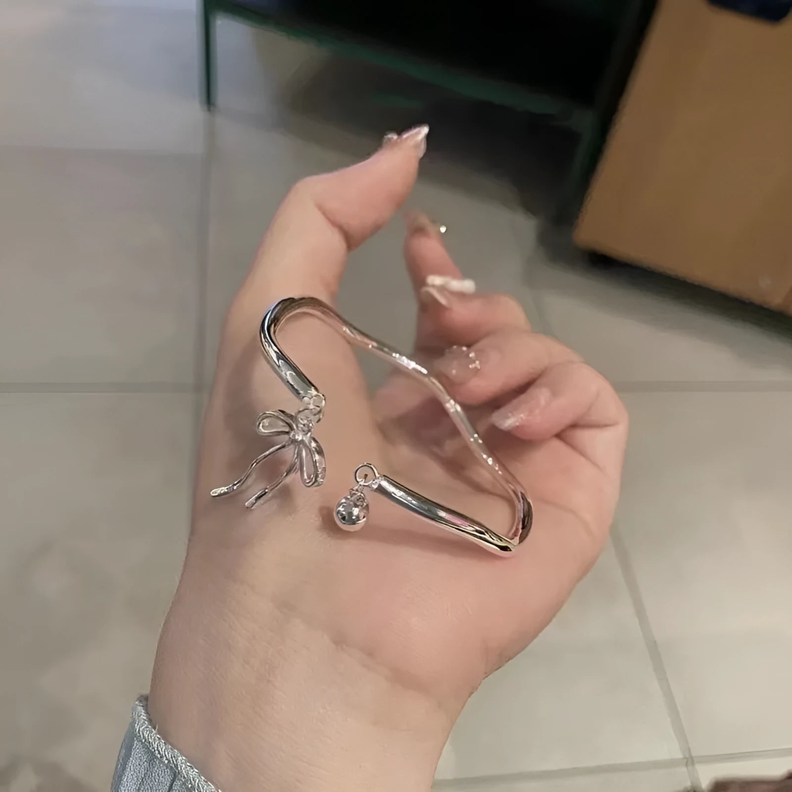 Silver adjustable bracelet with a detailed bow charm on a model's wrist, showing the adjustable clasp.