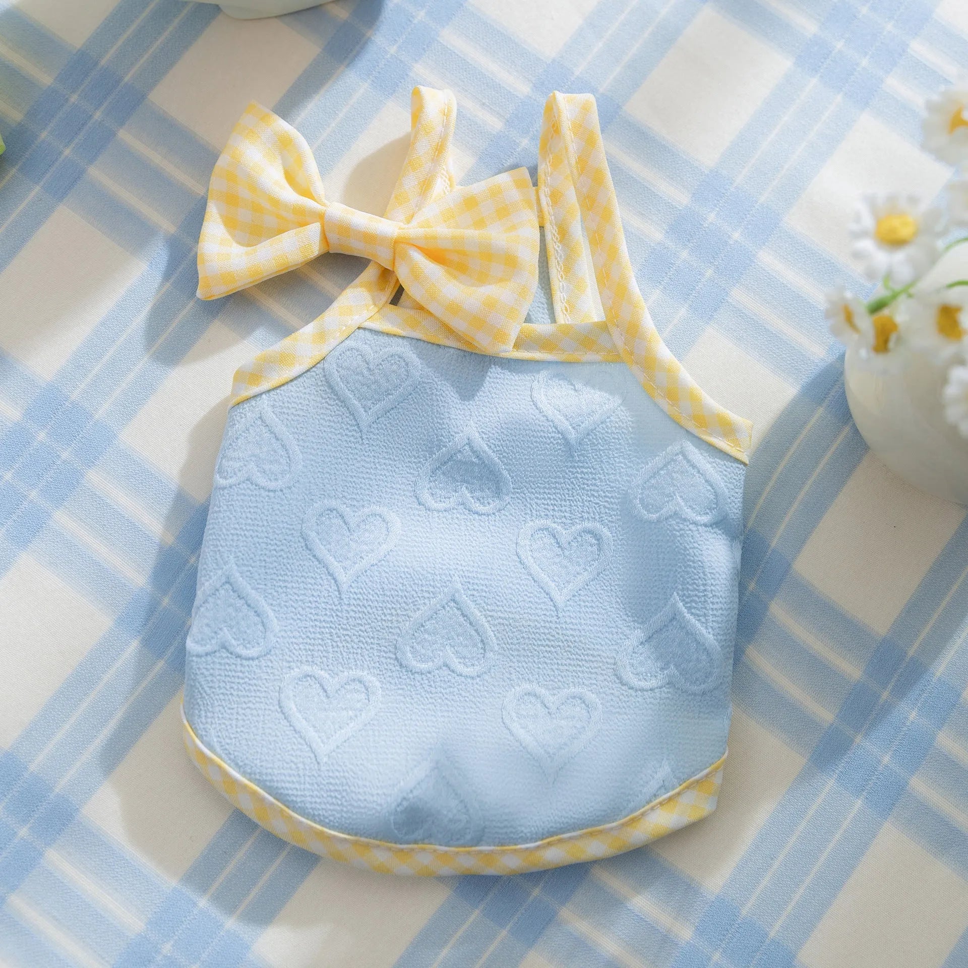 Small dog wearing a blue vest with heart texture and bow suspenders, showing adjustable elastic sides.
