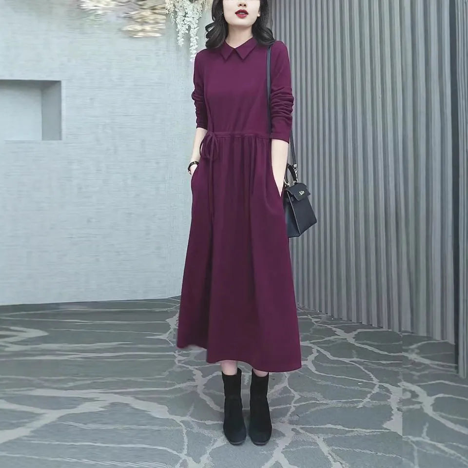 A woman wearing a solid purplish-red long-sleeve maxi dress, showcasing its extra-long sleeves and full-length skirt.