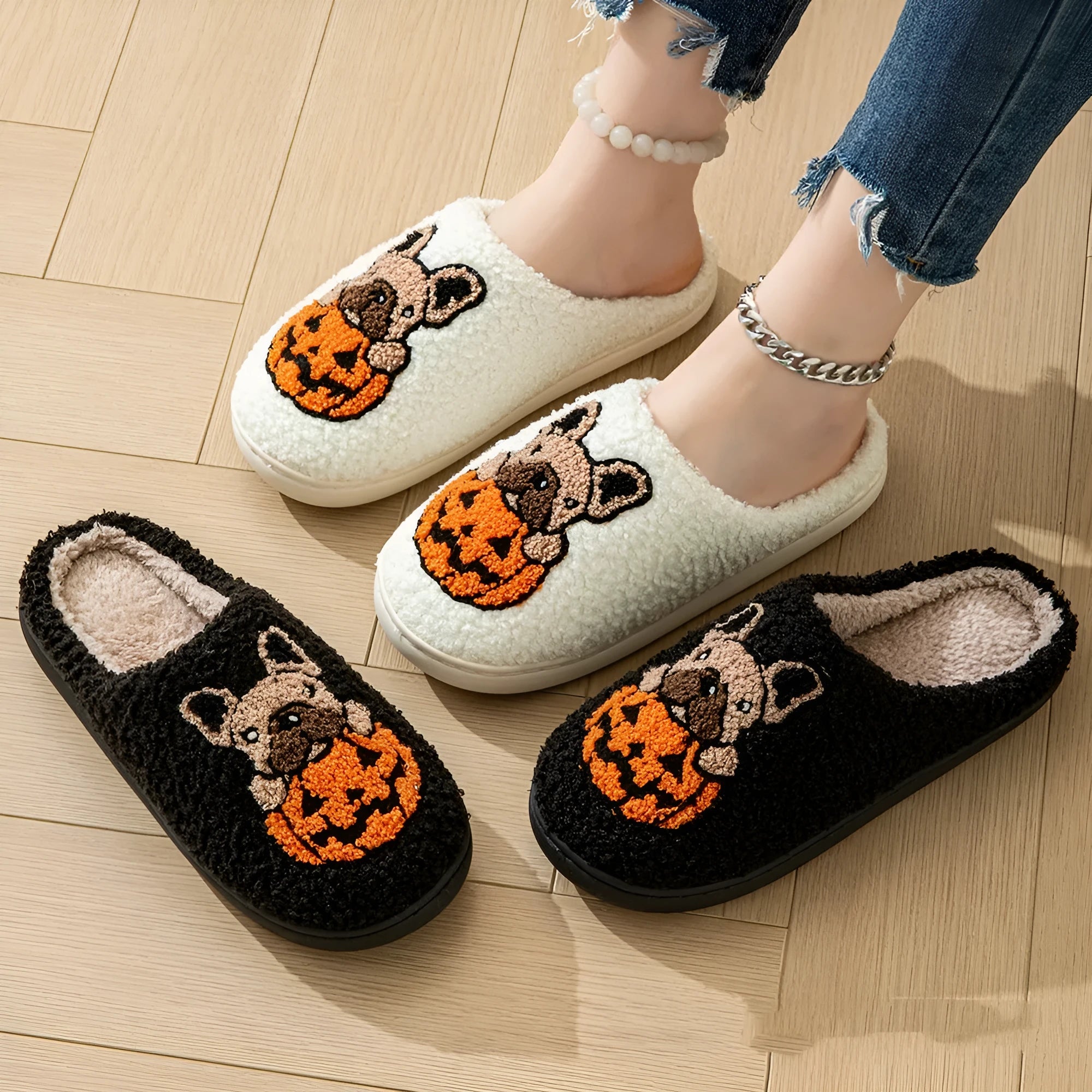 Black and white plush Halloween pumpkin slippers with textured rubber soles on a wooden floor.
