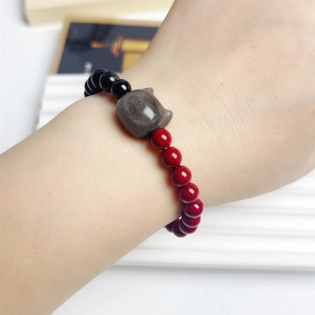 Obsidian crystal cat bracelet with colourful woven string band on a wrist.