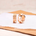 Close-up of a pair of rose gold circular hoop earrings with three small hollow heart shapes cut out of each band.