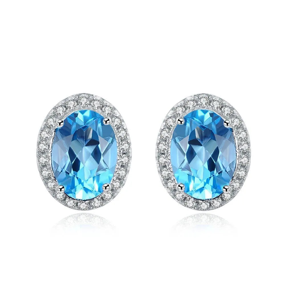 Four-piece sterling silver jewellery set with blue topaz gems: earrings, ring, pendant, and necklace on a geometry pattern.