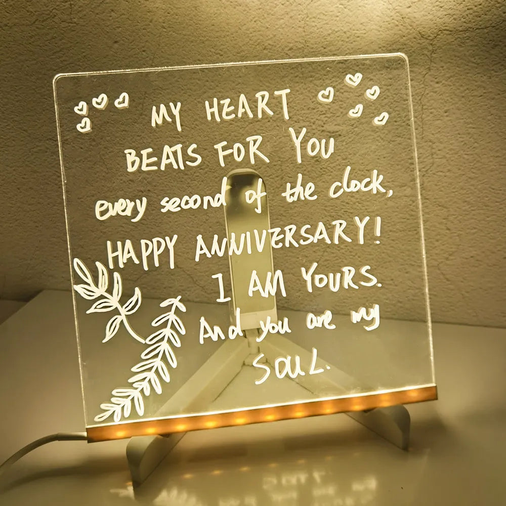 Acrylic DIY LED message board on a bracket, glowing softly with handwritten notes, alongside white and colourful pens.