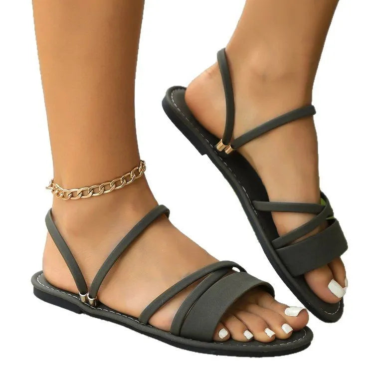 Women's black sandals with a flip-toe buckle and flat cross strap on a rubber sole.