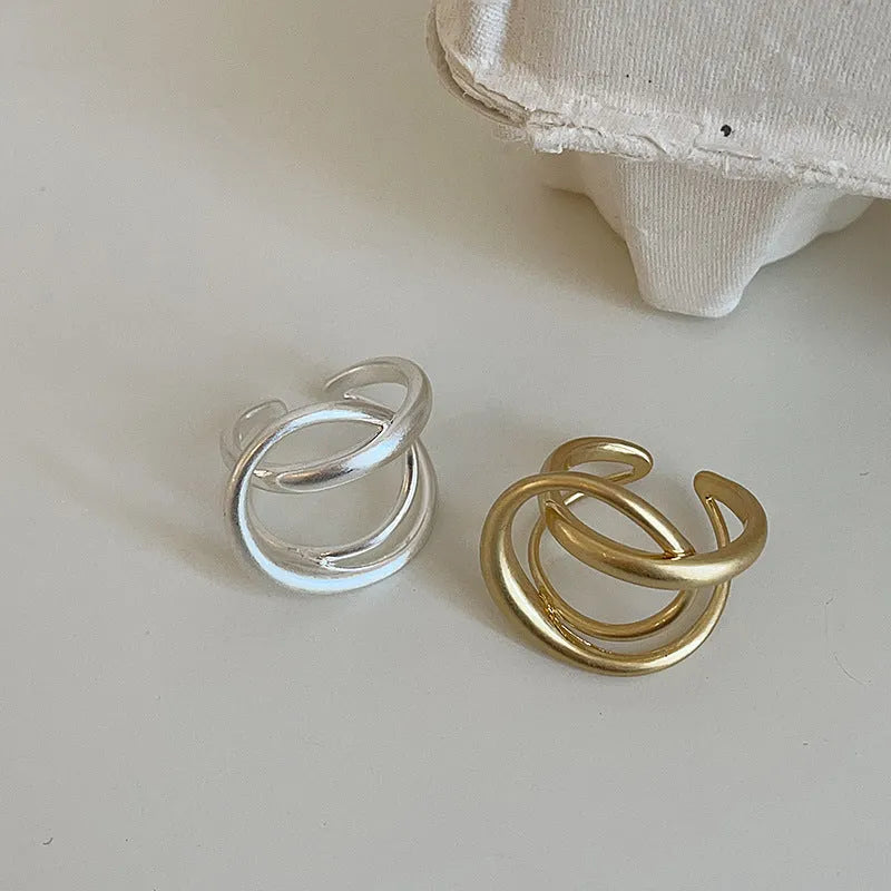 Geometric open ring with a 3D interlaced design in matte gold or silver metal.
