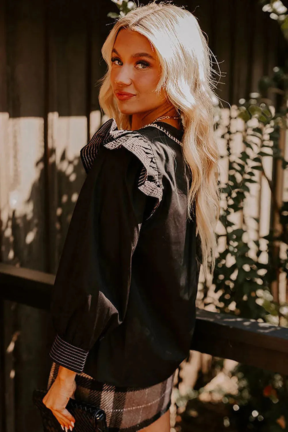 Black women's V-neck long sleeve blouse with white contrast stitching and a ruffle cuff detail