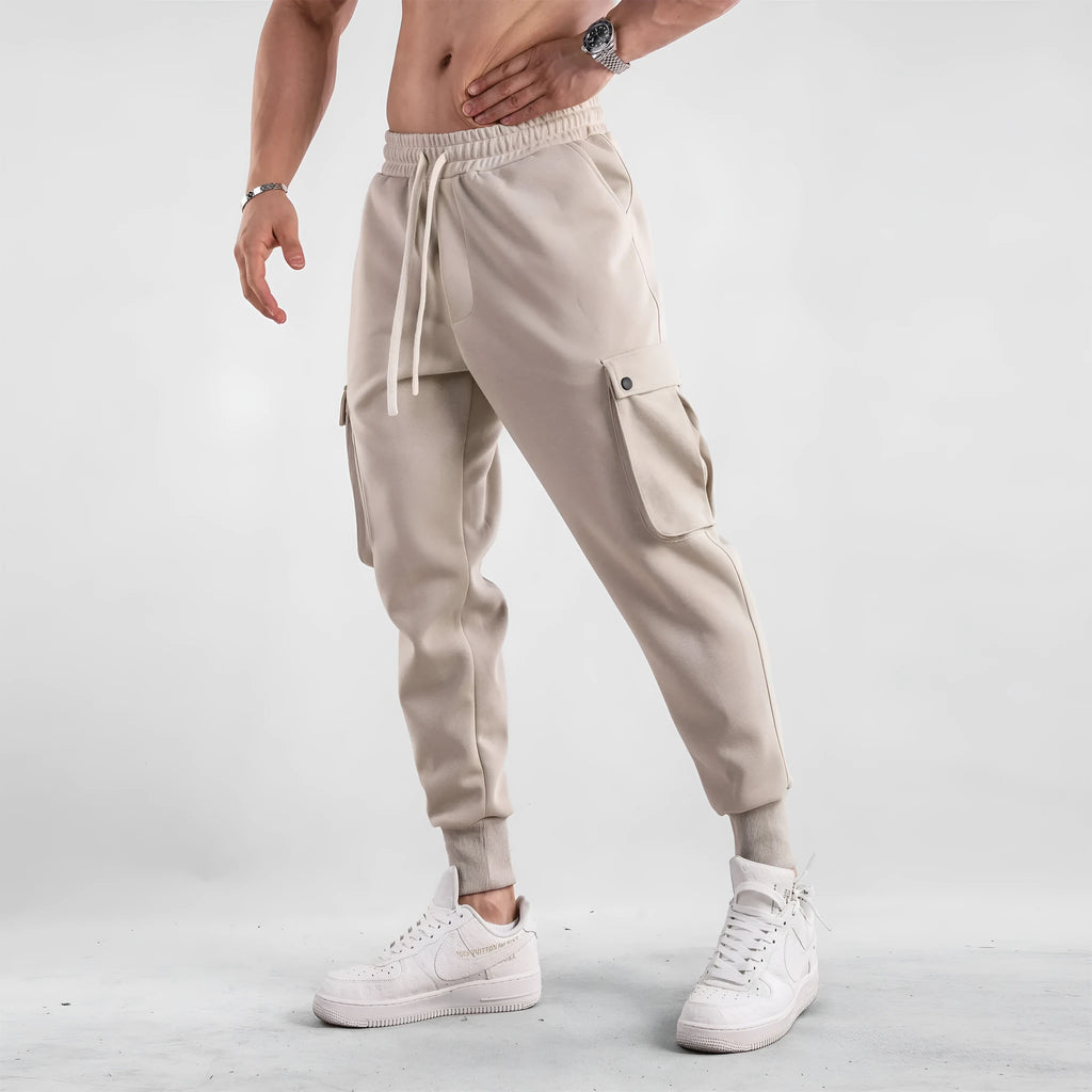 Men's loose-fit light grey cotton trousers with tapered legs and tied ankle cuffs, showing multi-pocket detail.
