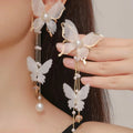 White butterfly-shaped dangling earrings with rhinestones, a pearl, and a fine chain on a plain background.