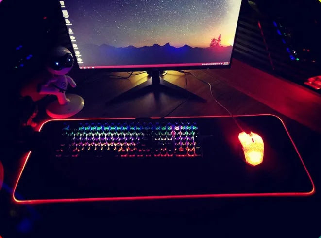 RGB luminous mouse pad with multi-colour LED lighting, fabric surface, and rubber base, shown on a desk with a mouse and keyboard