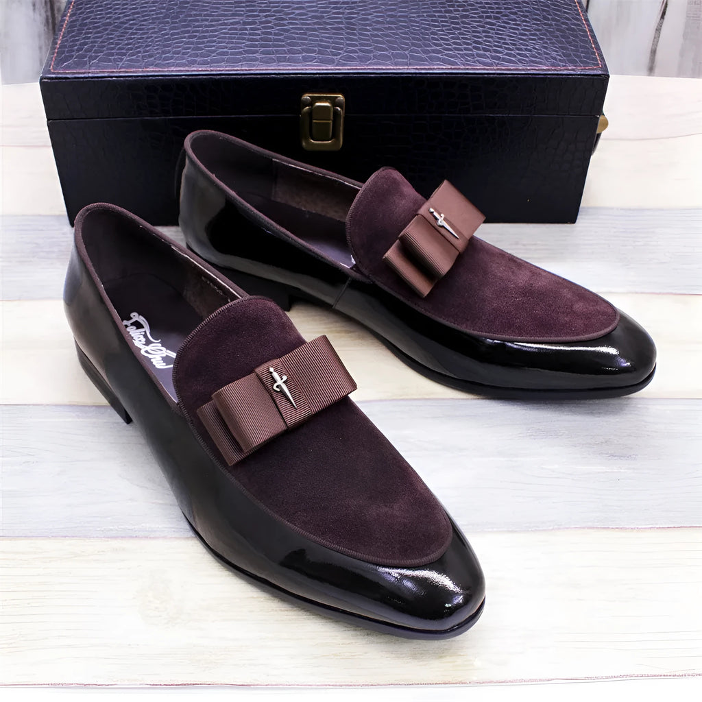 Men's black patent leather tassel loafers with a matte toe, shown on a wooden floor.