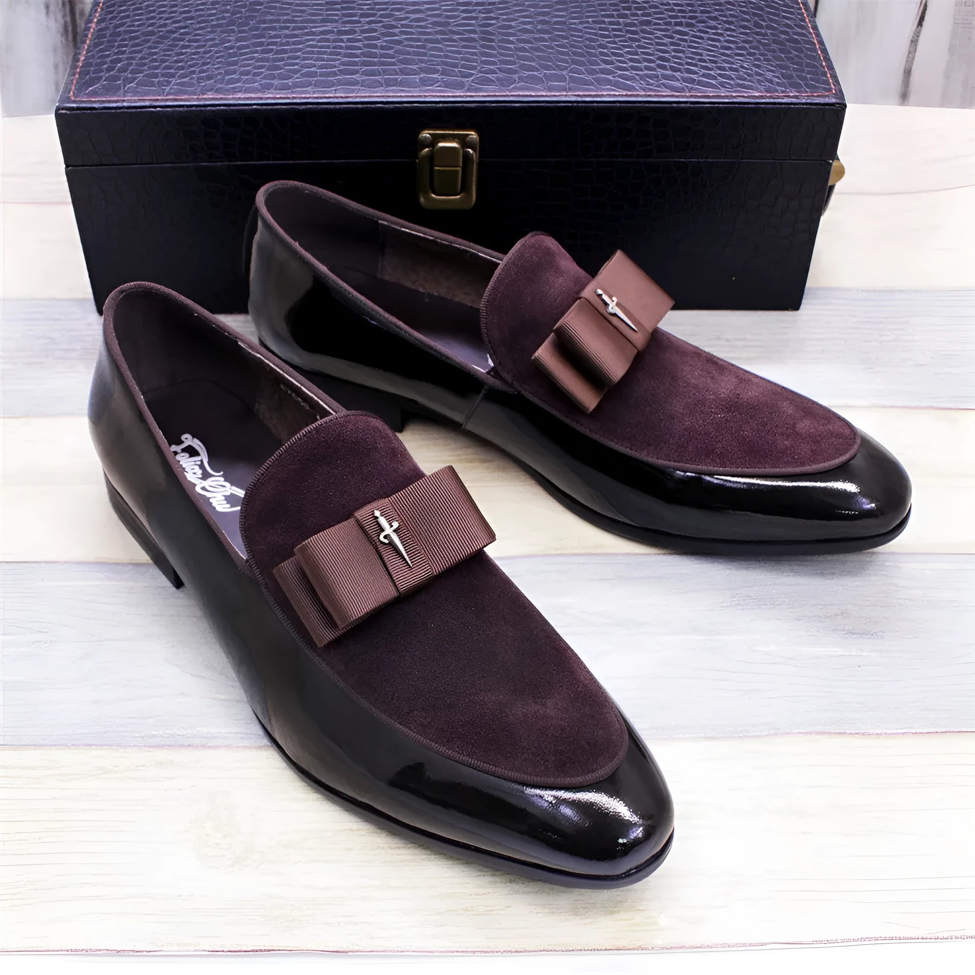 Men's black patent leather tassel loafers with a matte toe, shown on a wooden floor.