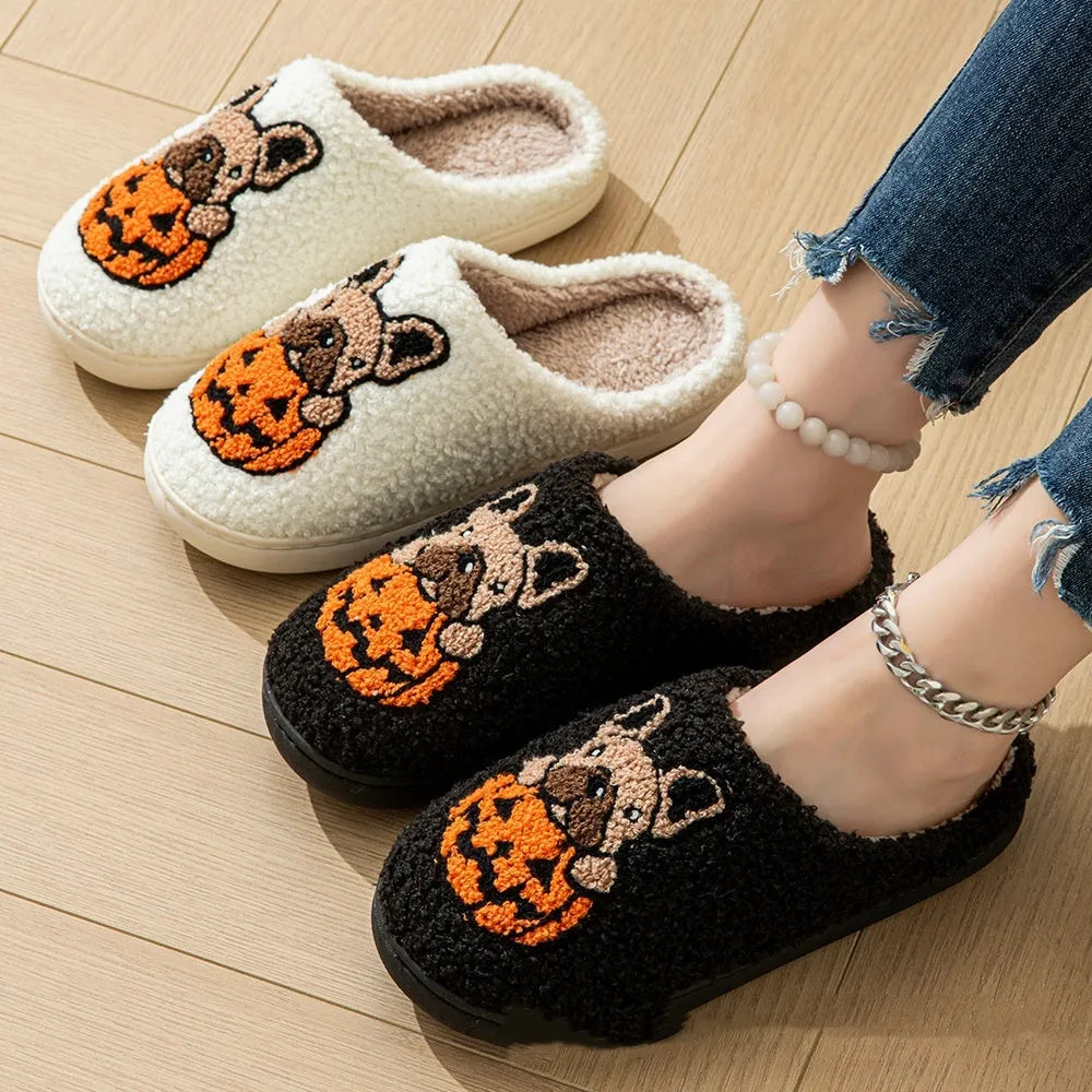 Black and white plush Halloween pumpkin slippers with textured rubber soles on a wooden floor.