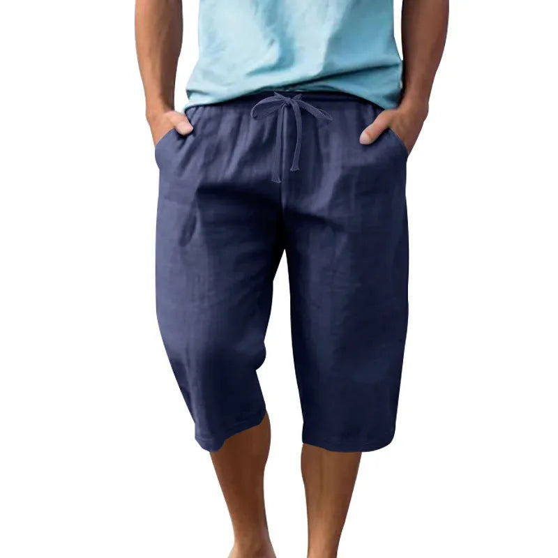 Man wearing loose-fit, solid-colour linen shorts in a light blue shade, showing the cropped length and drawstring waist.