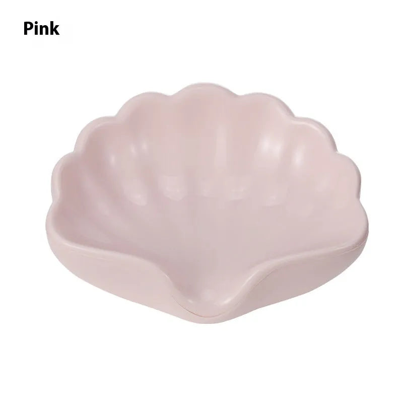 White or pink plastic shell-shaped soap dish for bathroom use on a counter.