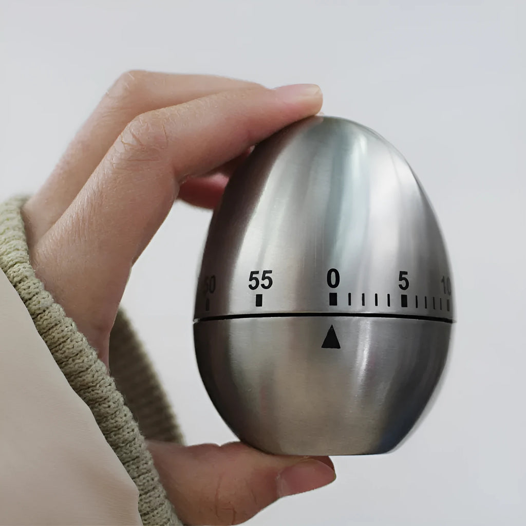 Stainless steel egg-shaped mechanical kitchen timer on a kitchen countertop